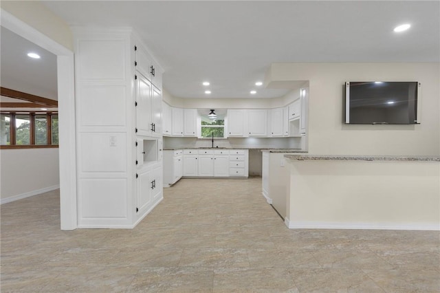 kitchen featuring light stone countertops, white cabinets, and sink