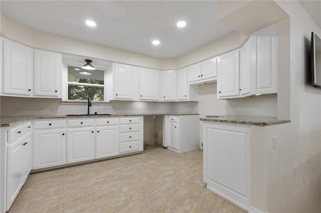 kitchen with white cabinets, light stone counters, and a sink