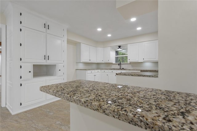 kitchen featuring recessed lighting, a sink, a peninsula, light stone counters, and white cabinetry