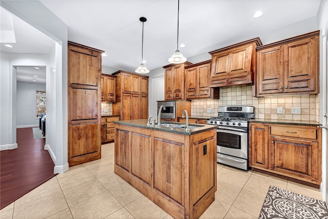 kitchen featuring a center island with sink, light tile patterned floors, hanging light fixtures, and stainless steel range with gas stovetop