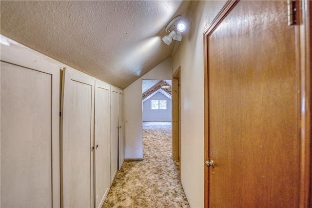 hallway with light colored carpet, a textured ceiling, and vaulted ceiling