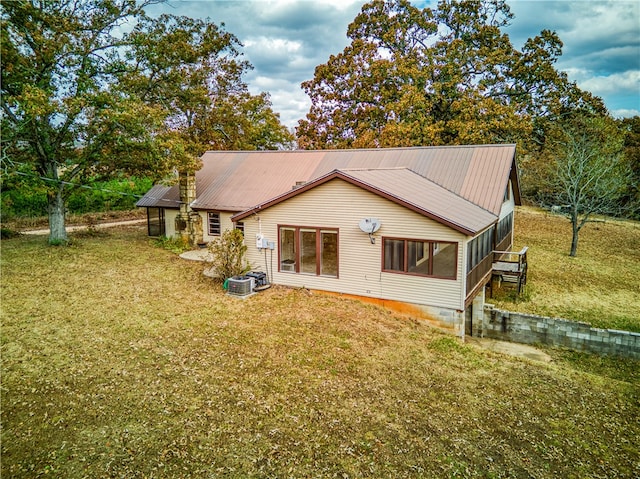 rear view of house with central AC unit, a sunroom, and a yard