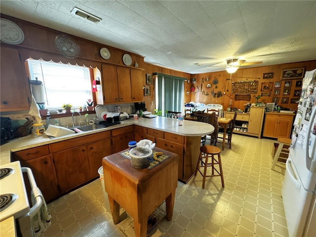 kitchen with sink, ceiling fan, a kitchen island, wooden walls, and white refrigerator