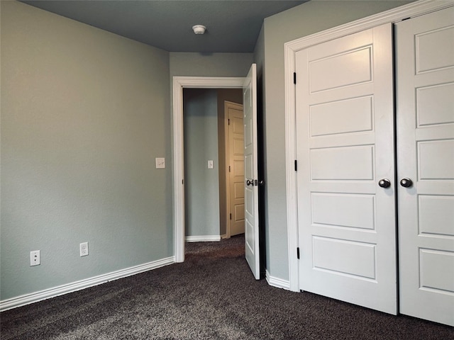 unfurnished bedroom with a closet and dark colored carpet