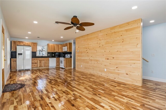 unfurnished living room featuring light wood-type flooring, wood walls, ceiling fan, and sink