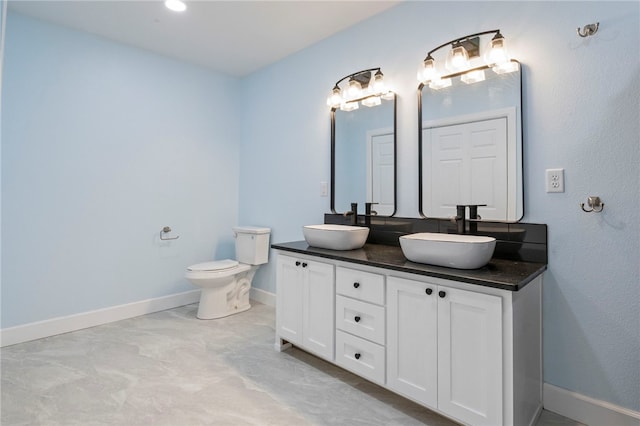 bathroom with double vanity, a sink, toilet, and baseboards