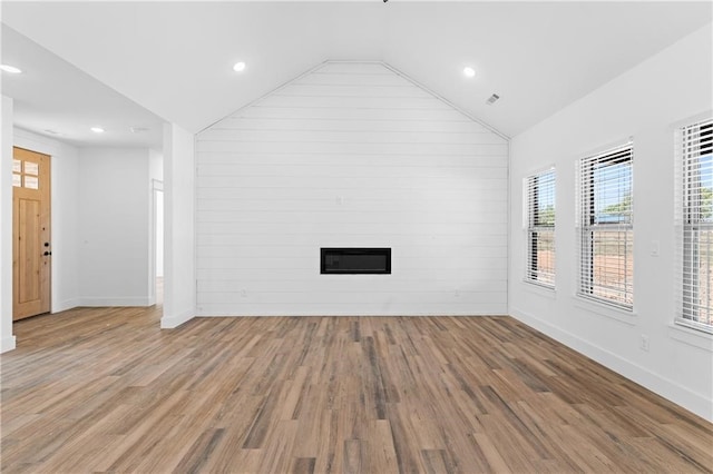 unfurnished living room featuring wooden walls, a fireplace, vaulted ceiling, and hardwood / wood-style flooring