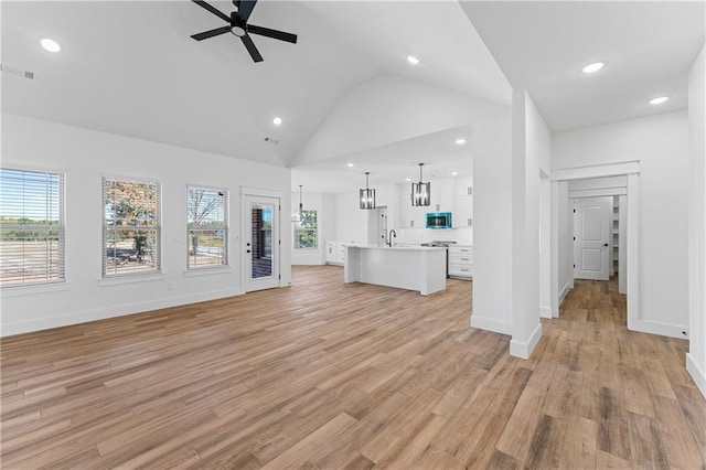 unfurnished living room with light hardwood / wood-style flooring, ceiling fan with notable chandelier, high vaulted ceiling, and a healthy amount of sunlight