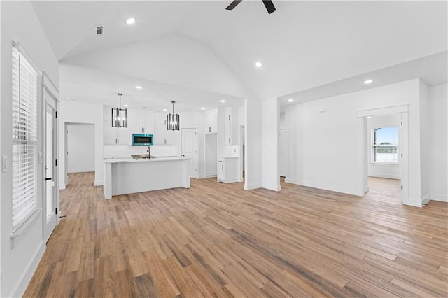 unfurnished living room featuring light hardwood / wood-style floors, high vaulted ceiling, ceiling fan, and sink