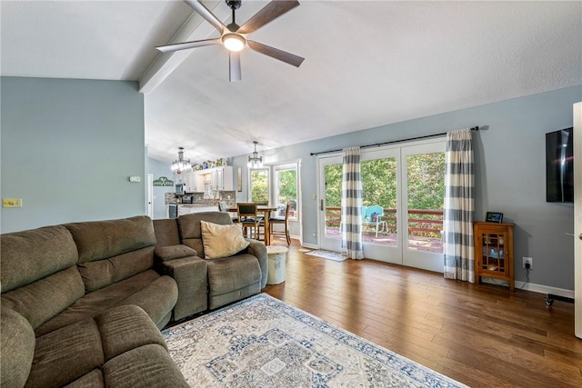 living room with ceiling fan with notable chandelier, vaulted ceiling with beams, wood finished floors, and baseboards