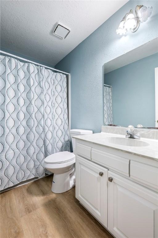 full bathroom with toilet, a textured ceiling, wood finished floors, vanity, and a textured wall