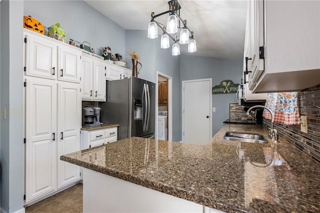 kitchen featuring a sink, dark stone countertops, stainless steel fridge, a peninsula, and white cabinets