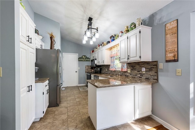 kitchen with decorative backsplash, dark stone countertops, a peninsula, freestanding refrigerator, and a sink