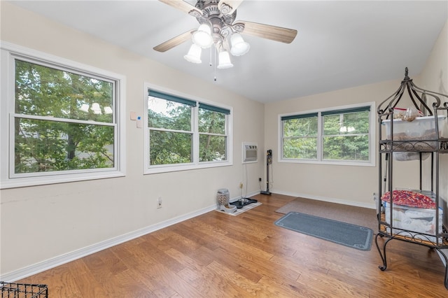 workout area featuring a healthy amount of sunlight, a wall mounted air conditioner, baseboards, and wood finished floors