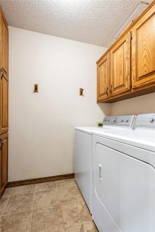 clothes washing area with baseboards, cabinet space, a textured ceiling, and washing machine and clothes dryer