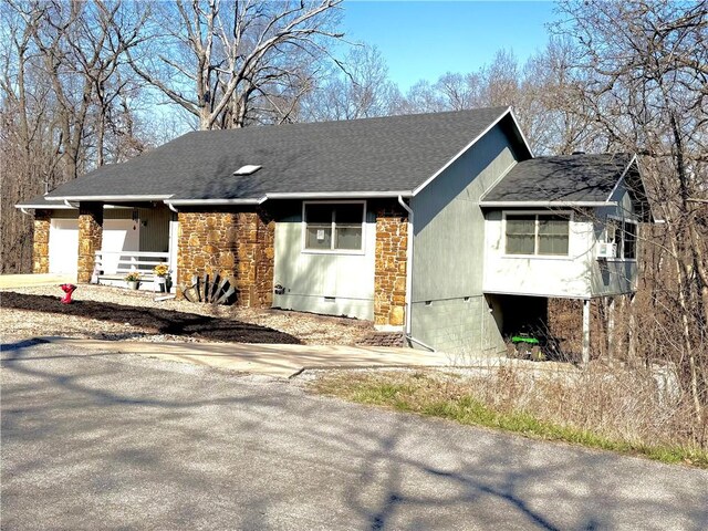 view of side of home with stone siding and a shingled roof