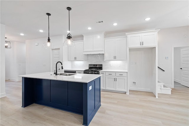 kitchen with sink, white cabinets, an island with sink, hanging light fixtures, and gas range