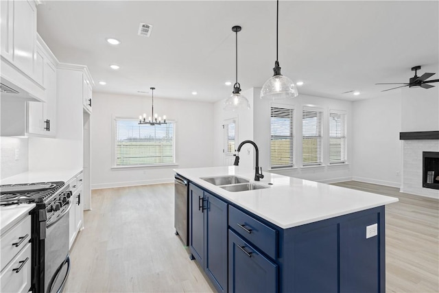 kitchen featuring sink, white cabinets, gas range oven, blue cabinetry, and a center island with sink