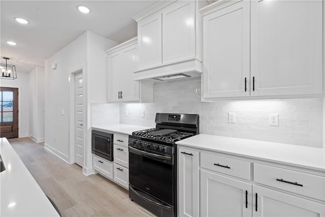 kitchen with white cabinets, light hardwood / wood-style floors, pendant lighting, a chandelier, and black appliances