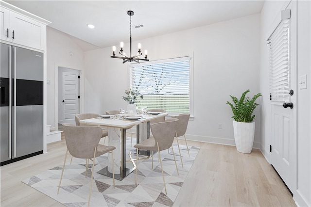 dining space with lofted ceiling, a notable chandelier, and light hardwood / wood-style flooring