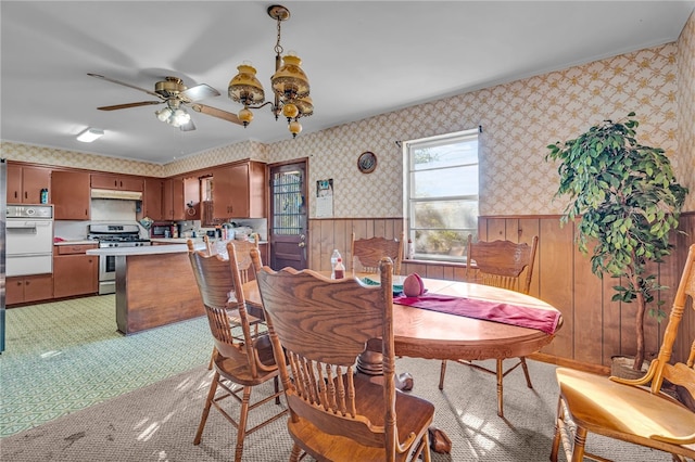 carpeted dining area with ceiling fan and wooden walls