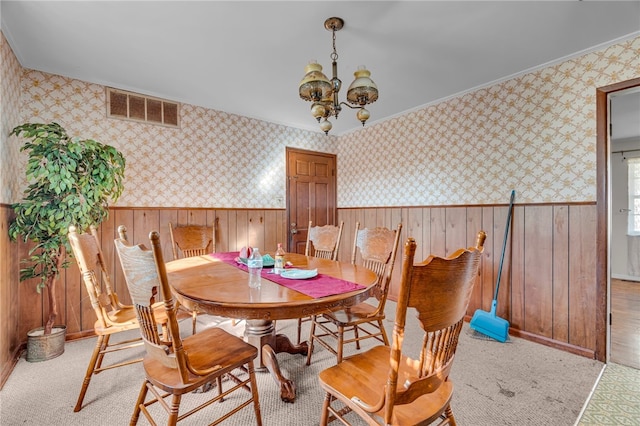 dining space featuring wood walls, crown molding, and an inviting chandelier