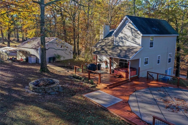 rear view of property featuring a wooden deck, a carport, a hot tub, and a fire pit