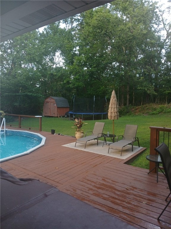 outdoor pool with a trampoline, an outbuilding, a storage unit, a lawn, and a wooden deck