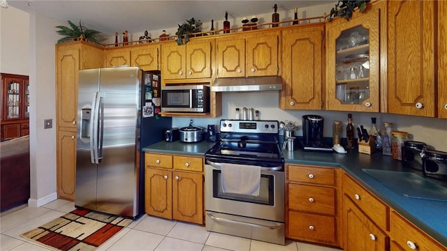 kitchen with brown cabinets, under cabinet range hood, light tile patterned floors, and stainless steel appliances