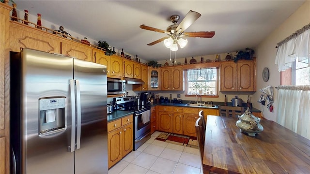 kitchen with brown cabinets, appliances with stainless steel finishes, a healthy amount of sunlight, a sink, and under cabinet range hood