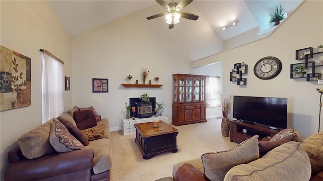 living area with ceiling fan, high vaulted ceiling, a wood stove, and light colored carpet