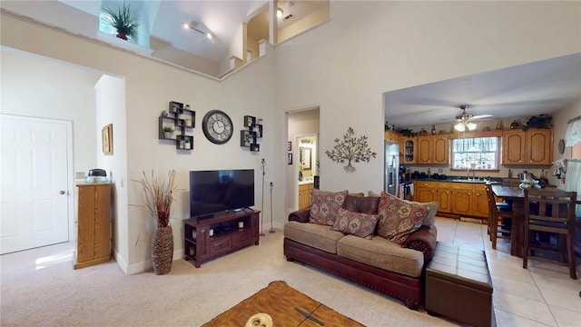 living room featuring light tile patterned floors, a towering ceiling, light carpet, ceiling fan, and baseboards