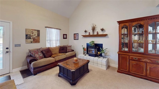 living area featuring light carpet, a wood stove, baseboards, and high vaulted ceiling