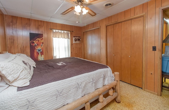 bedroom with multiple closets, ceiling fan, wooden walls, and light colored carpet