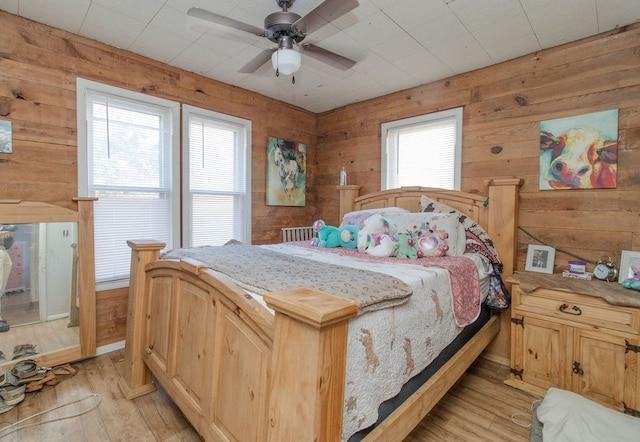 bedroom with light hardwood / wood-style floors, multiple windows, and wood walls