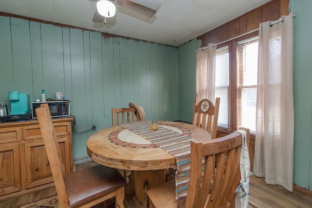 dining space with wood walls, ceiling fan, and light hardwood / wood-style floors