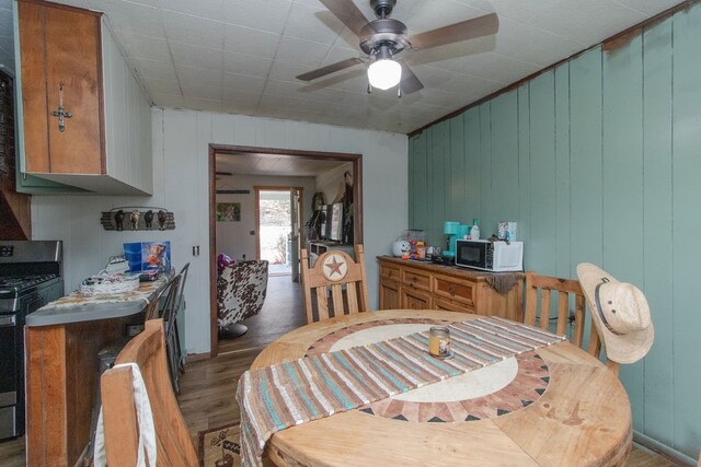 dining space featuring ceiling fan, wood walls, and light wood-type flooring