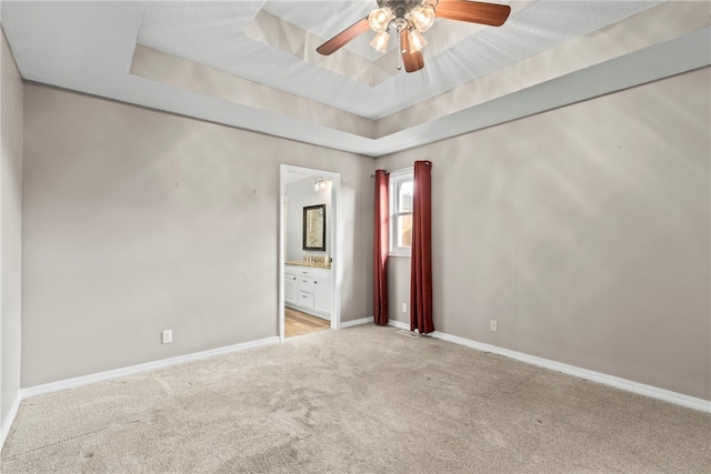 spare room featuring light carpet, a raised ceiling, and ceiling fan