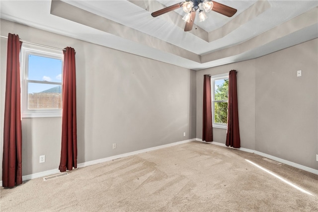 carpeted empty room with a raised ceiling and ceiling fan