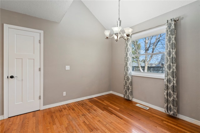 unfurnished room featuring a textured ceiling, light hardwood / wood-style floors, lofted ceiling, and a notable chandelier