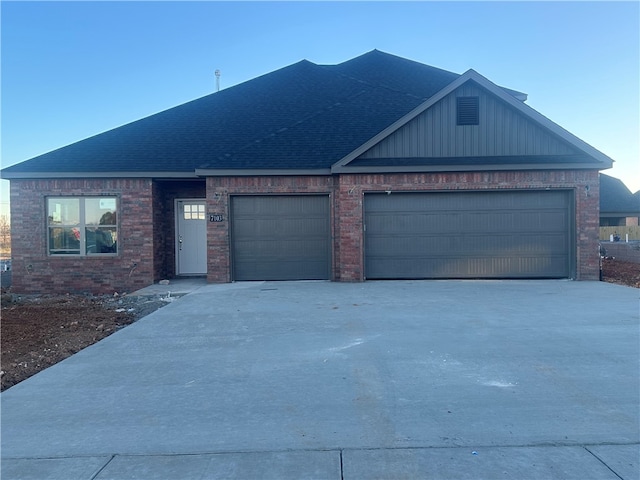 view of front of home with an attached garage, driveway, a shingled roof, and brick siding