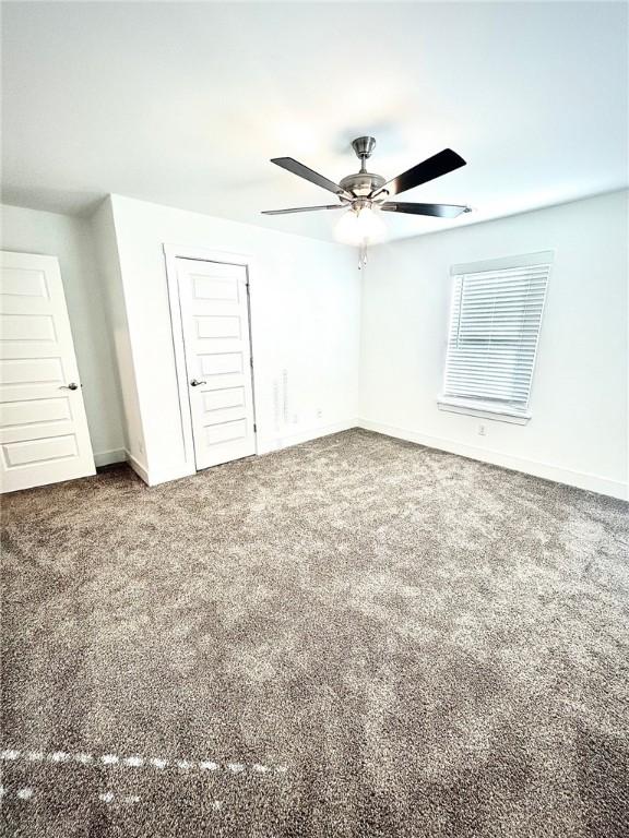 carpeted spare room featuring baseboards and a ceiling fan