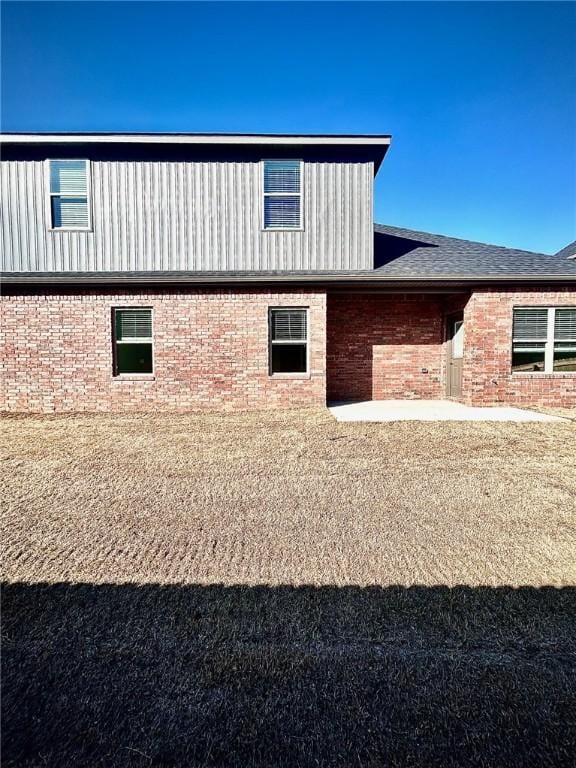 view of side of home with roof with shingles, a patio, and brick siding