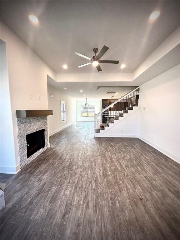 unfurnished living room featuring stairs, baseboards, dark wood-type flooring, and a stone fireplace