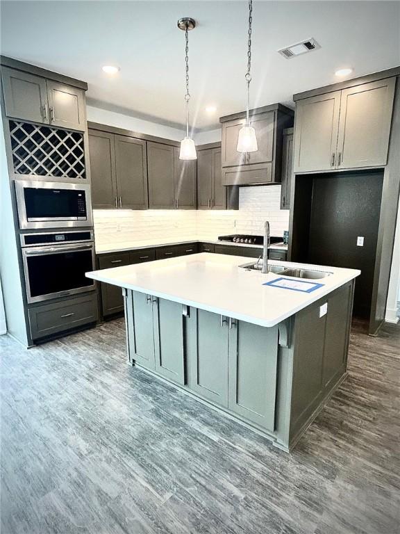 kitchen featuring a center island with sink, stainless steel appliances, visible vents, a sink, and wood finished floors