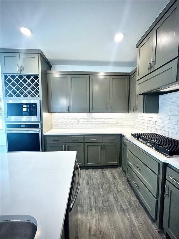 kitchen featuring light countertops, appliances with stainless steel finishes, dark wood finished floors, and decorative backsplash