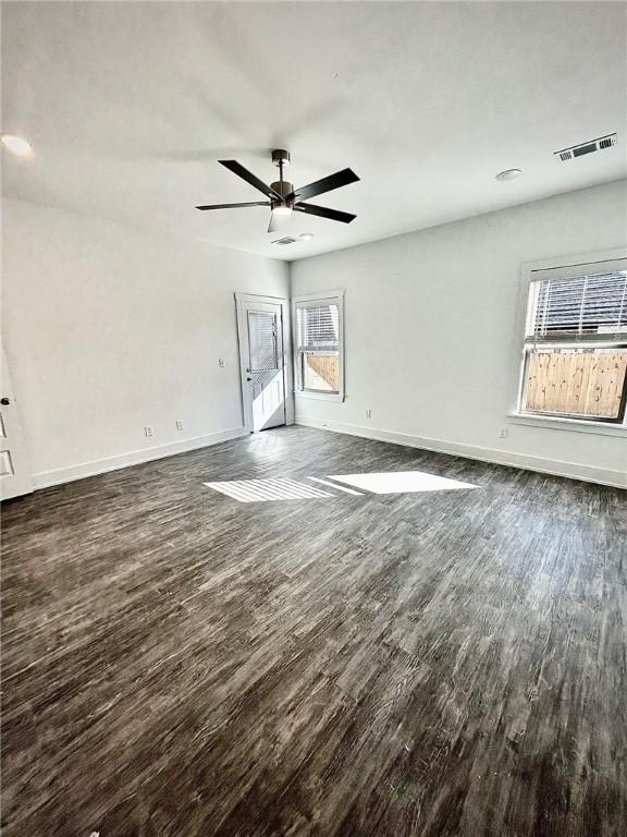 empty room featuring a ceiling fan, visible vents, dark wood finished floors, and baseboards