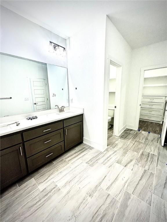 bathroom featuring toilet, a sink, baseboards, a closet, and double vanity