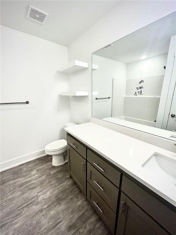 bathroom with visible vents, toilet, vanity, wood finished floors, and baseboards