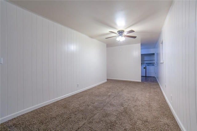 carpeted empty room featuring ceiling fan, washer and clothes dryer, and wooden walls